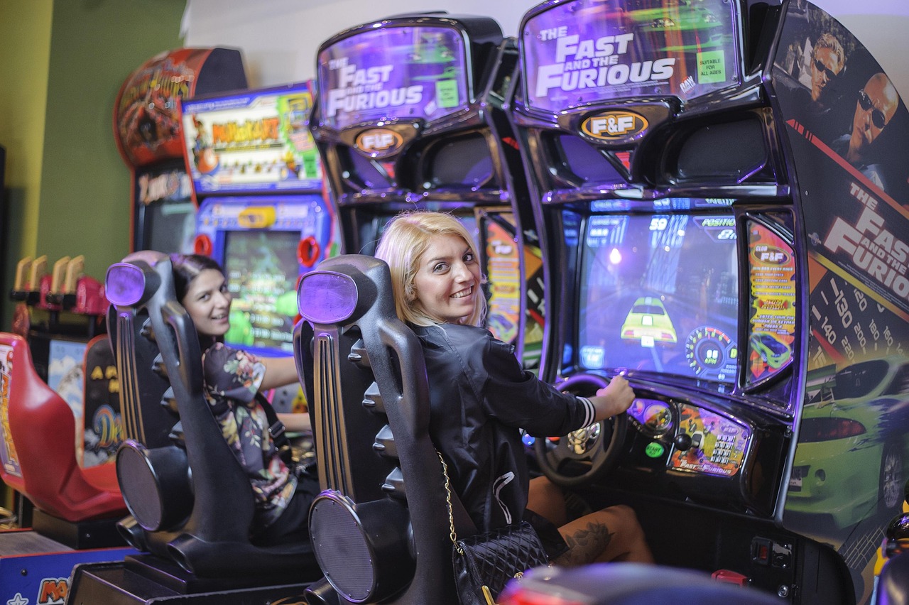 Two kids side by side on racing simulator seats, gripping the wheels